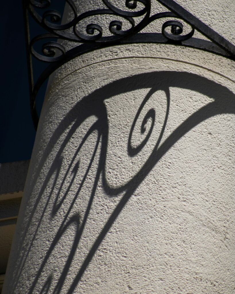 Shadow of an ornate iron railing on a textured stucco wall